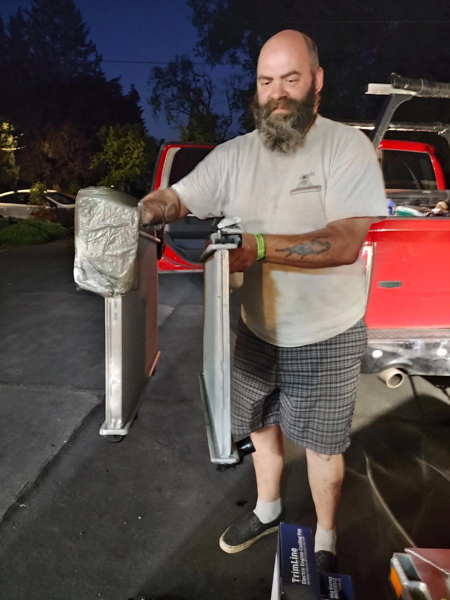 Dave holding up the Two Honda Accord Radiators from the Lemons Accordian. One is a thin $50 single core ebay radiator, and the other is a parts store $200 two core radiator, and obviously quite superior for cooling.